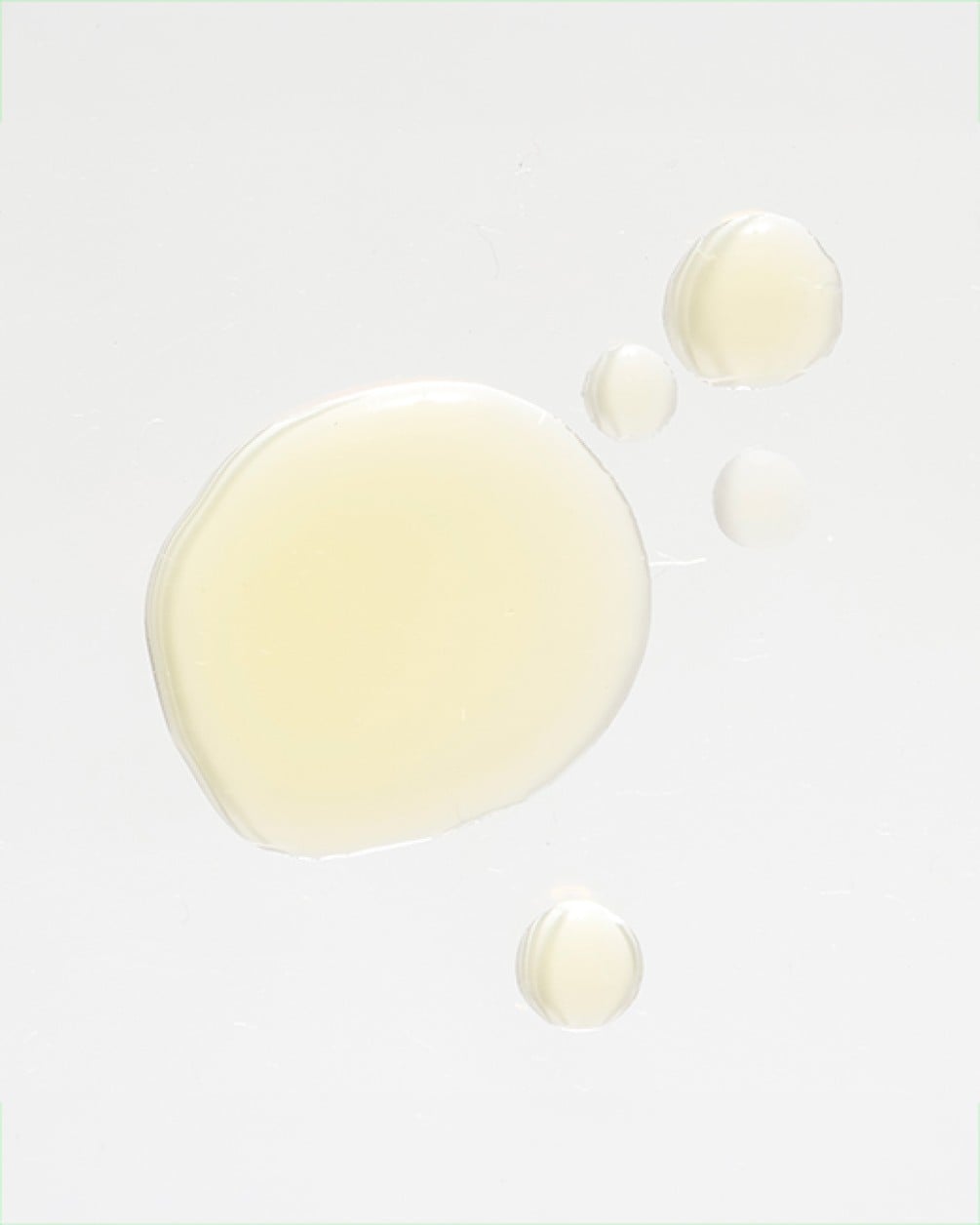 A top-down view of several yellow, translucent droplets of liquid collagen scattered on a clean white surface.