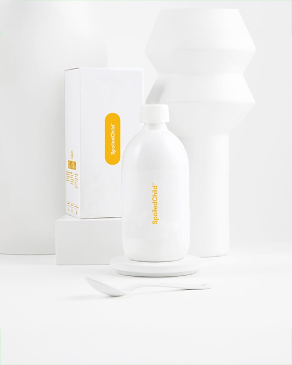 A minimalist lifestyle shot featuring the white SpoiledChild pineapple liquid collagen bottle and its product box arranged against a clean, white geometric background.
