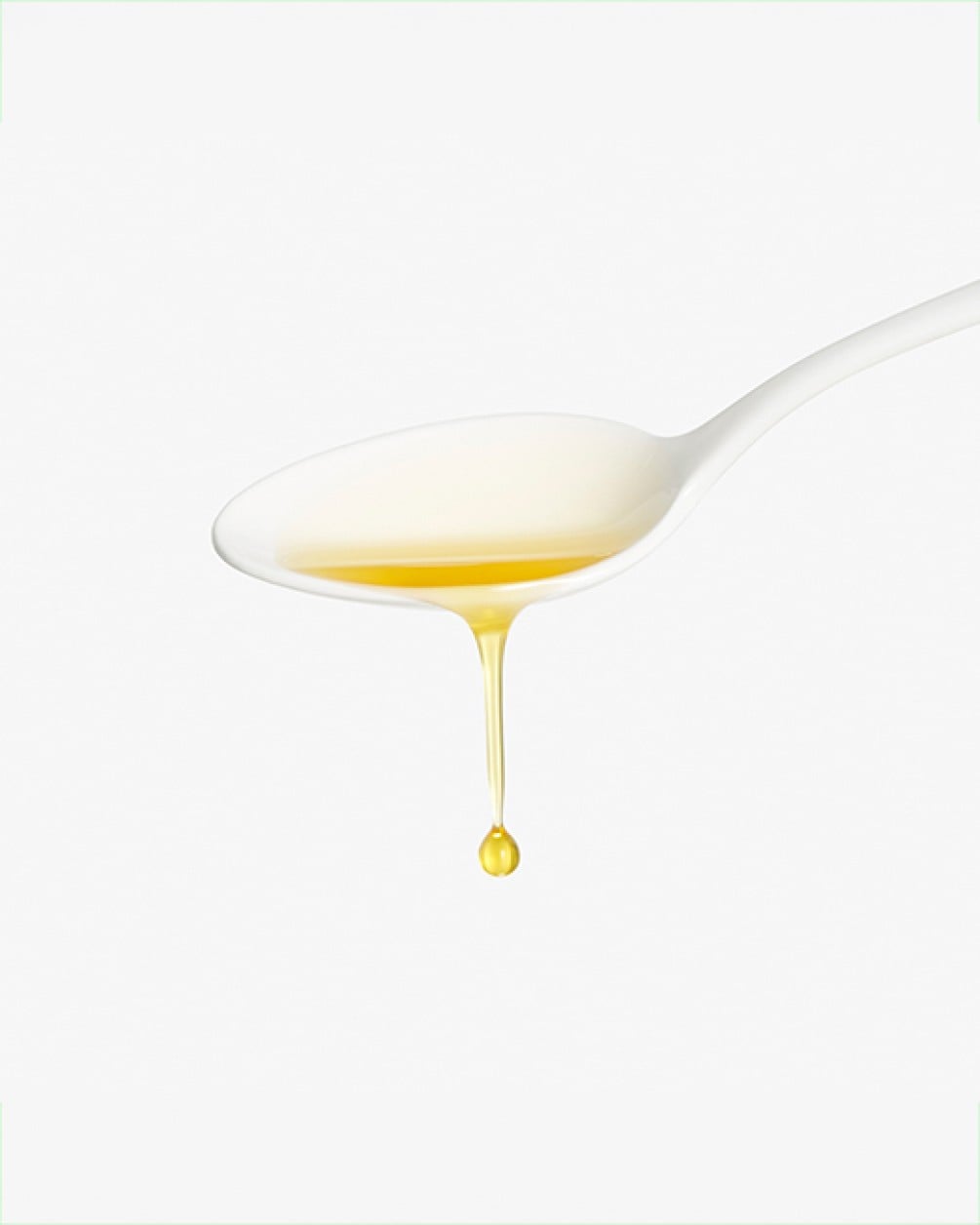 A close-up of a white spoon holding yellow liquid collagen, with a single drop dripping from the bottom against a white background.